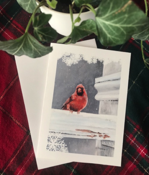 A holiday card featuring a cardinal sitting on a white picket fence. 